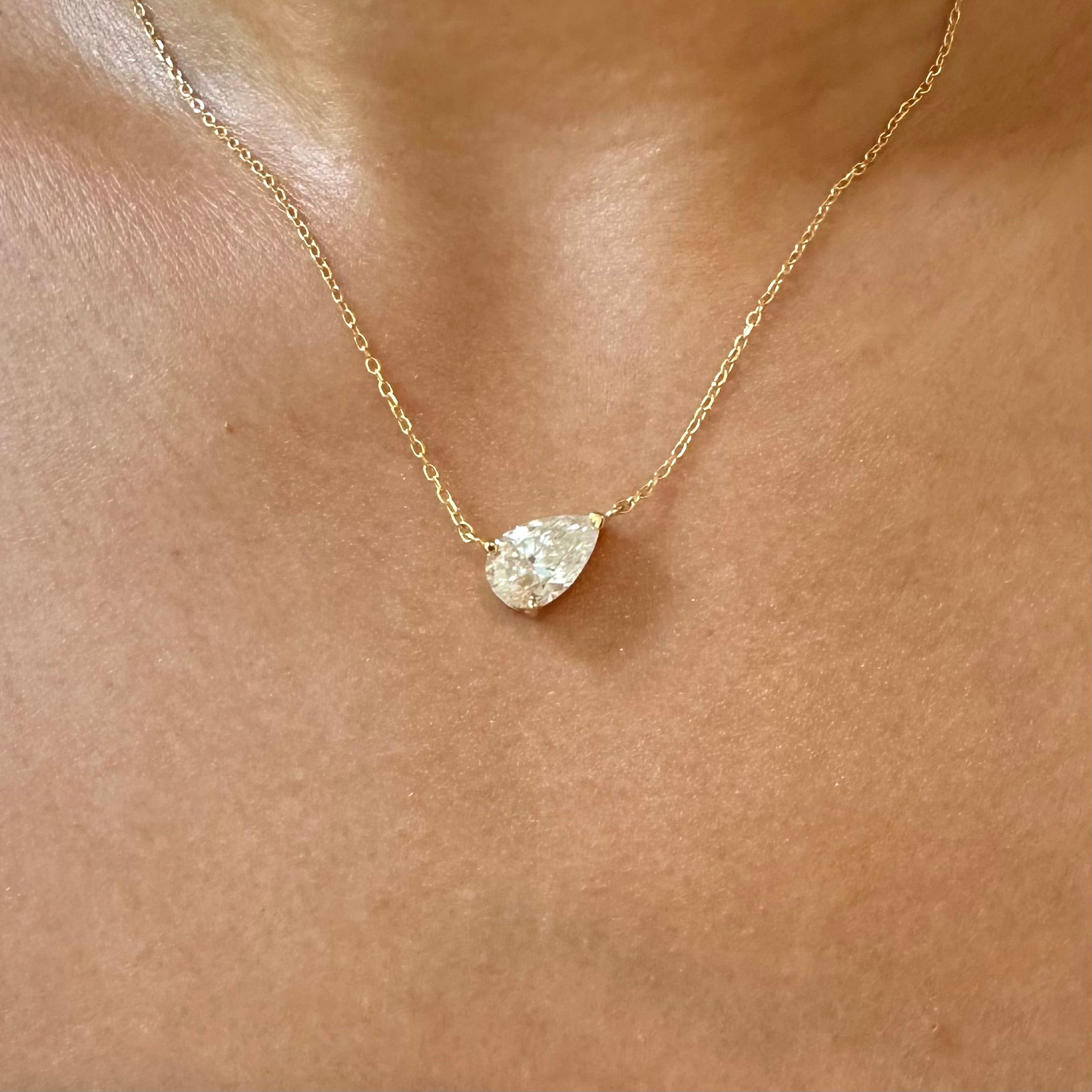 A close-up of a delicate gold chain necklace worn on a person's neck, featuring a pear-shaped clear gemstone pendant.